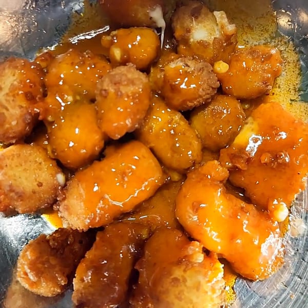 Close-up of golden-brown fried cheese curds coated in a glistening orange sauce, with melted cheese visible.