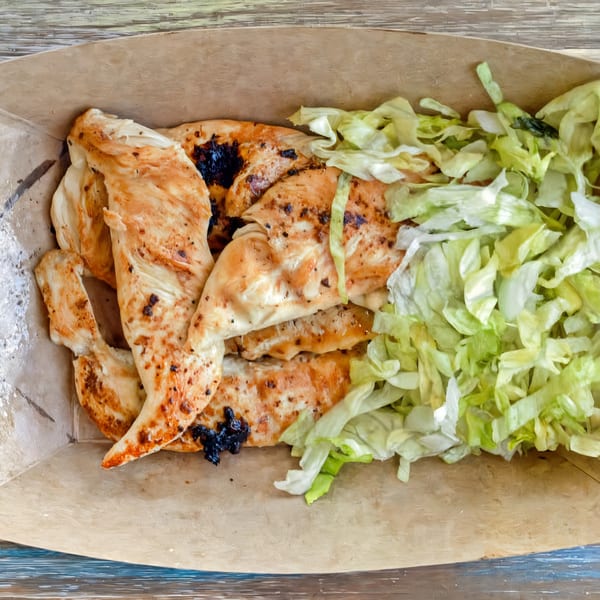 Grilled chicken strips and shredded lettuce in a brown paper container from Brake Burger Garage.