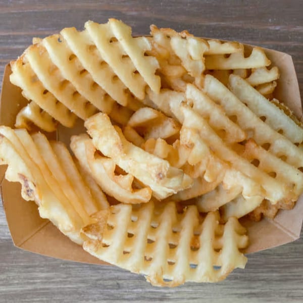 Golden brown waffle fries in a paper tray, on a wooden table.