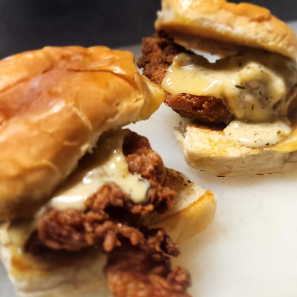 Two Brake Burger Garage sliders with fried chicken and creamy sauce on a white surface.