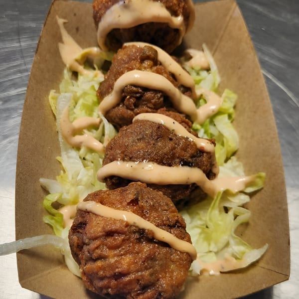 Four crispy fried burger bites with sauce and shredded lettuce in a cardboard tray.