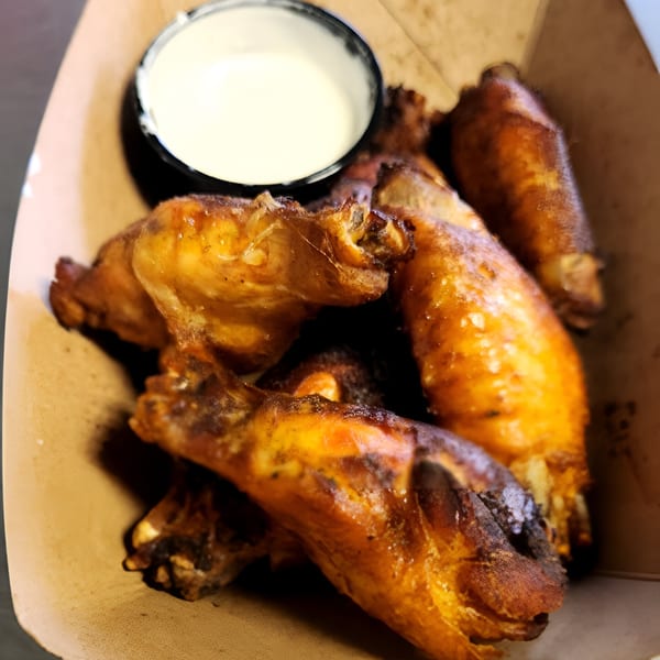 Crispy golden-brown chicken wings with a side of white dipping sauce in a cardboard container.