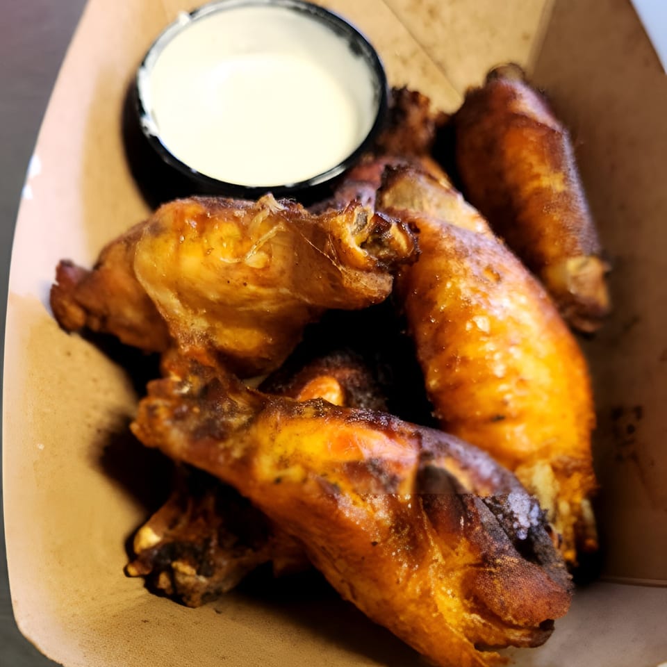 Crispy golden-brown chicken wings with a side of white dipping sauce in a cardboard container.