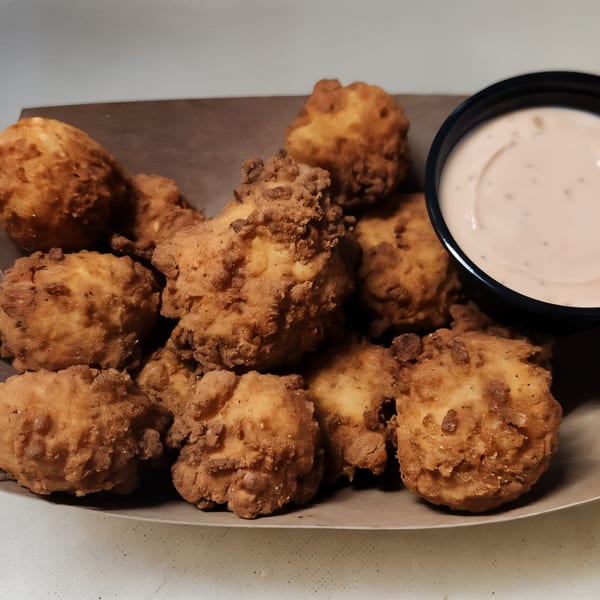 A plate of golden-brown fried cheese curds with a side of dipping sauce.