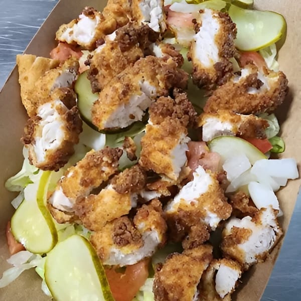 Crispy fried chicken pieces, pickles, tomatoes, and lettuce in a brown paper container.