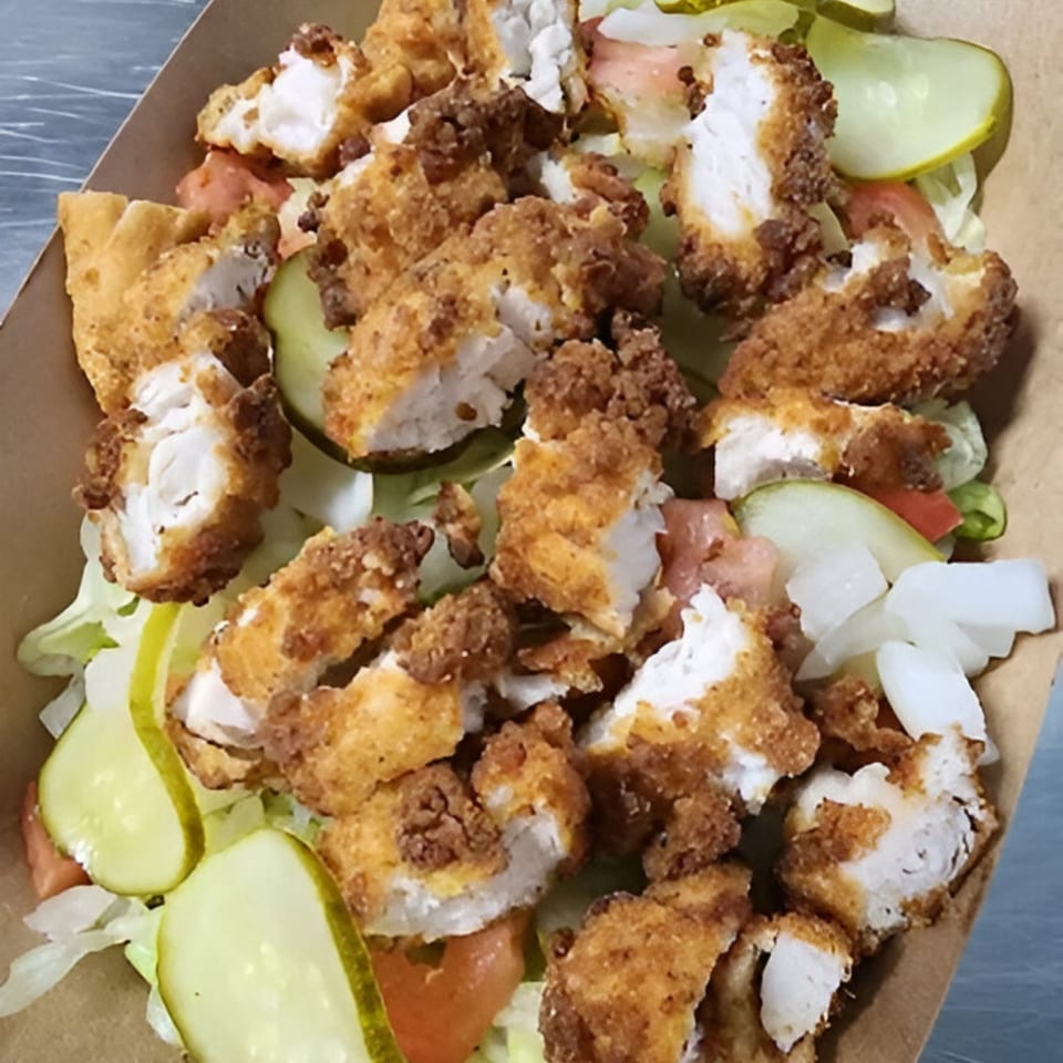 Crispy fried chicken pieces, pickles, tomatoes, and lettuce in a brown paper container.